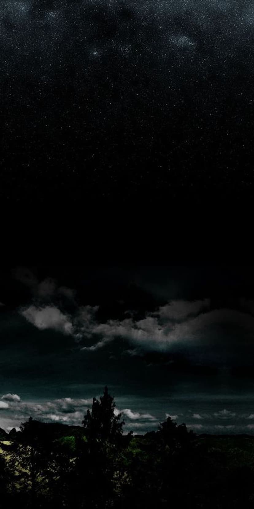 Millions of stars illuminate the dark sky over heavy clouds and a silhouetted forest landscape at night.