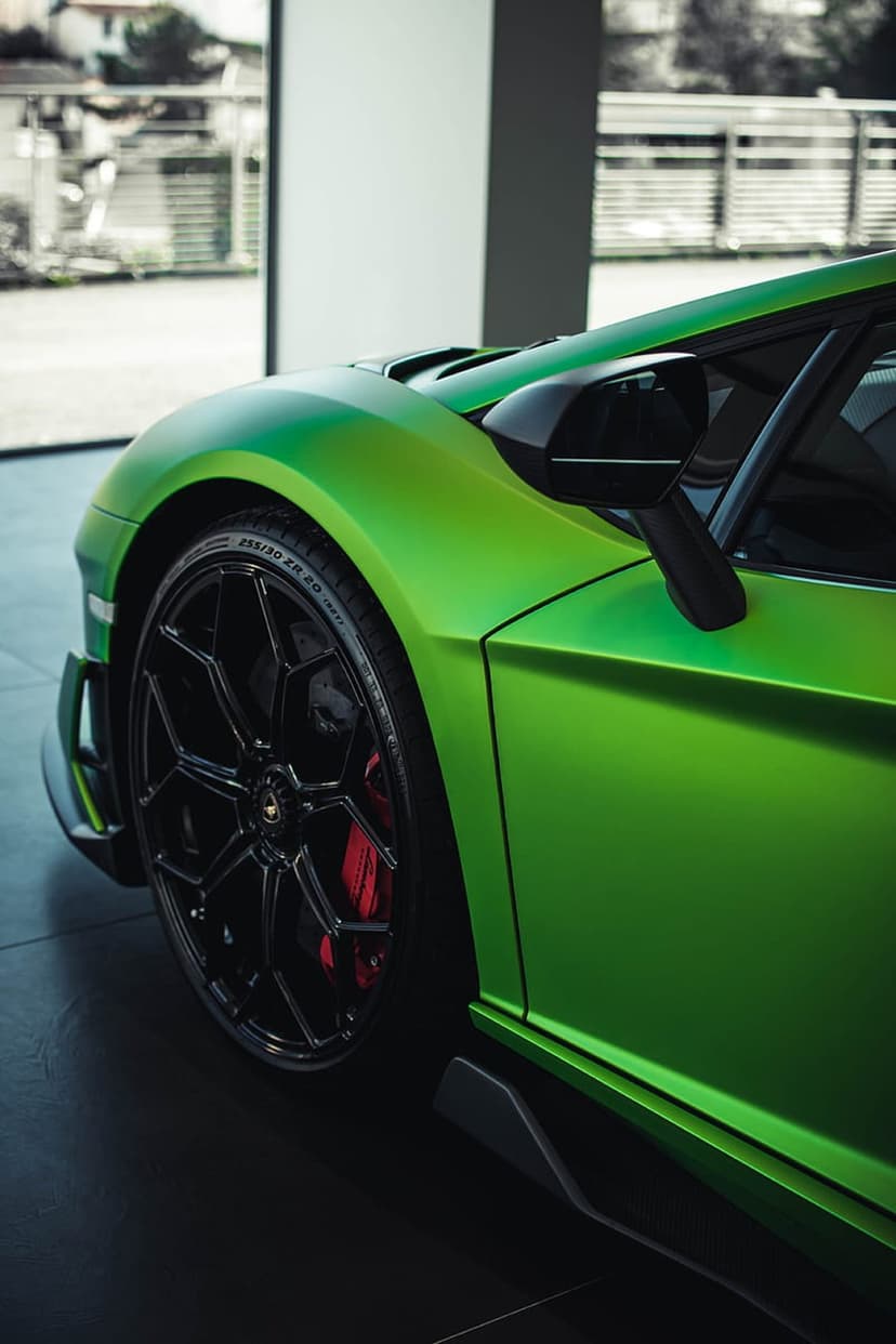 Lamborghini Aventador front wheel with black rims and red brake calipers on a matte lime green supercar fender.
