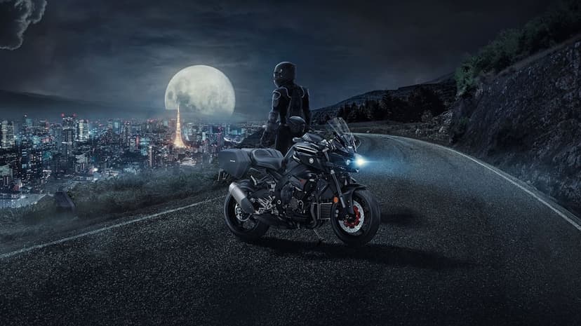 Black Yamaha motorcycle and rider on a night road overlooking a massive moon and glowing city skyline.