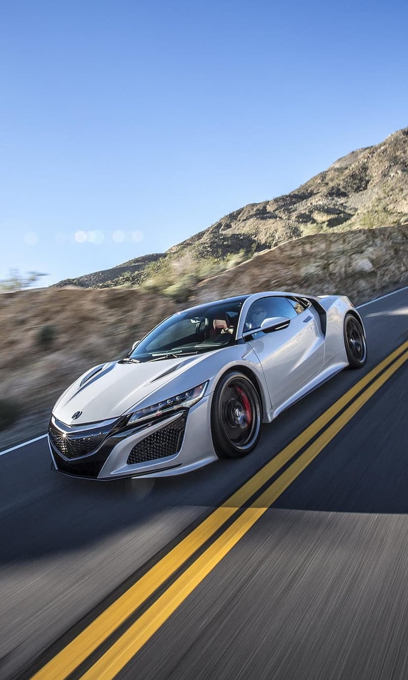 Silver Acura NSX supercar speeding on a desert highway with motion blur, mountains, and blue sky background.