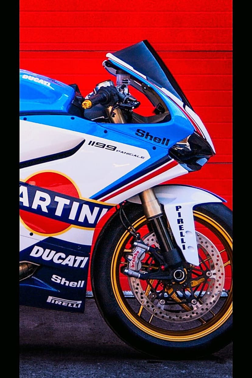 Ducati 1199 Panigale motorcycle with Martini racing stripes, gold front rim, and Brembo brakes on a red background.