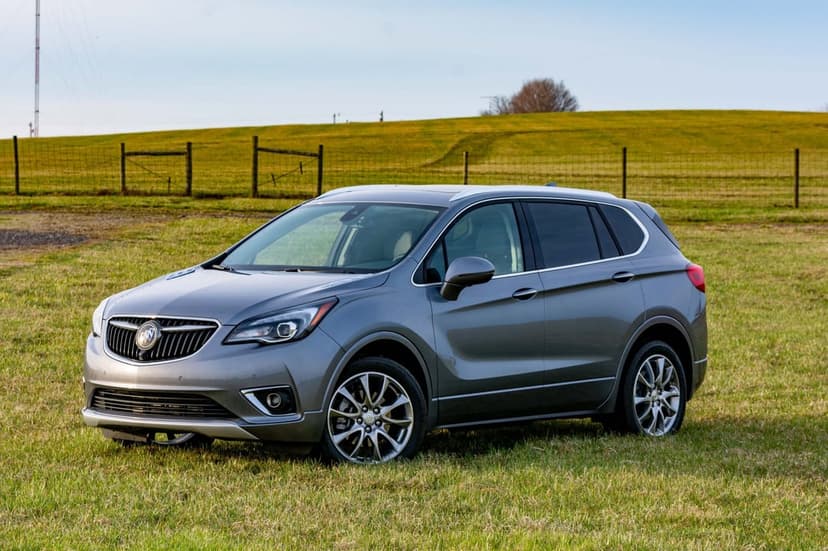 Metallic gray Buick Envision SUV parked on a green field with rolling hills and a clear sky background.