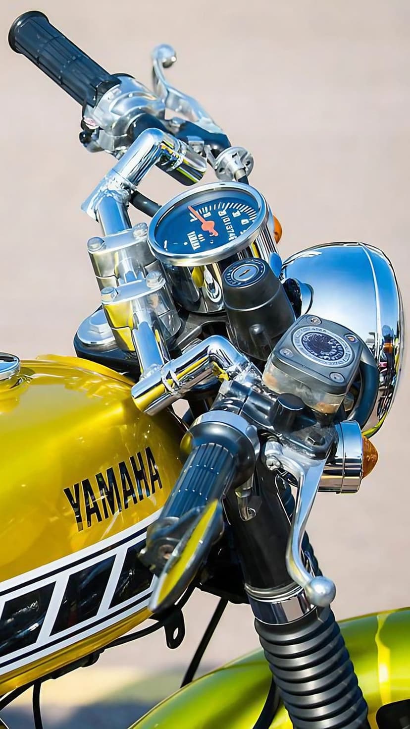 Yellow Yamaha motorcycle handlebars with a chrome speedometer, black handgrips, and reflective fuel tank logo.