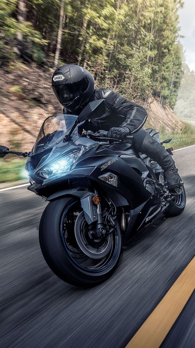 Kawasaki Ninja ZX-6R rider leaning into a forest turn with glowing headlights and motion-blurred trees.