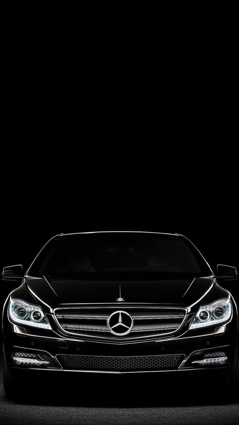 Black Mercedes-Benz sedan with a chrome grille and glowing LED headlights against a dark, moody background.