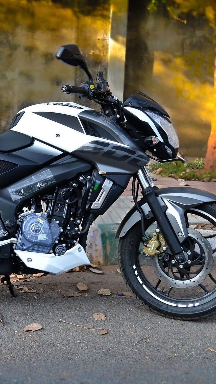 Bajaj Pulsar NS200 motorcycle in white and grey with a sharp headlight and front disc brake against a wall.