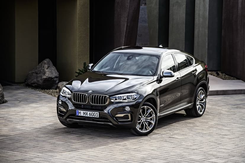 Black BMW X6 luxury SUV parked on stone pavers in front of modern geometric architectural pillars.