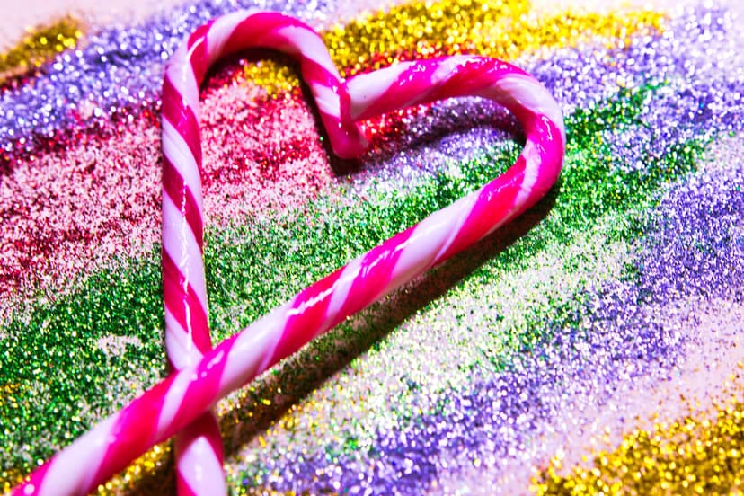 Candy cane heart with pink stripes rests on a vibrant surface of sparkling multi-colored rainbow glitter.