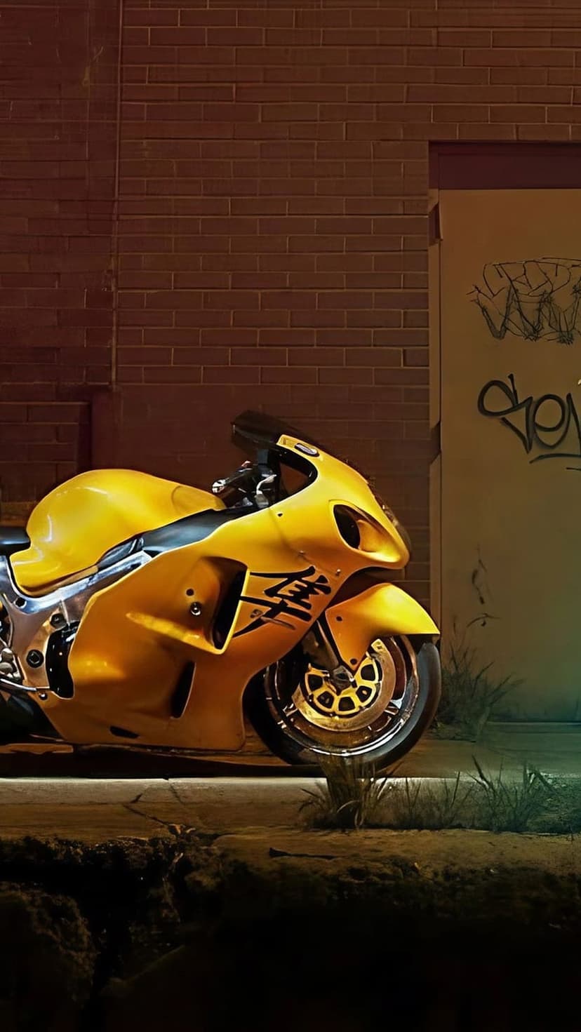 Yellow Suzuki Hayabusa sportbike parked by a brick wall with graffiti and grass in a low-angle vertical shot.