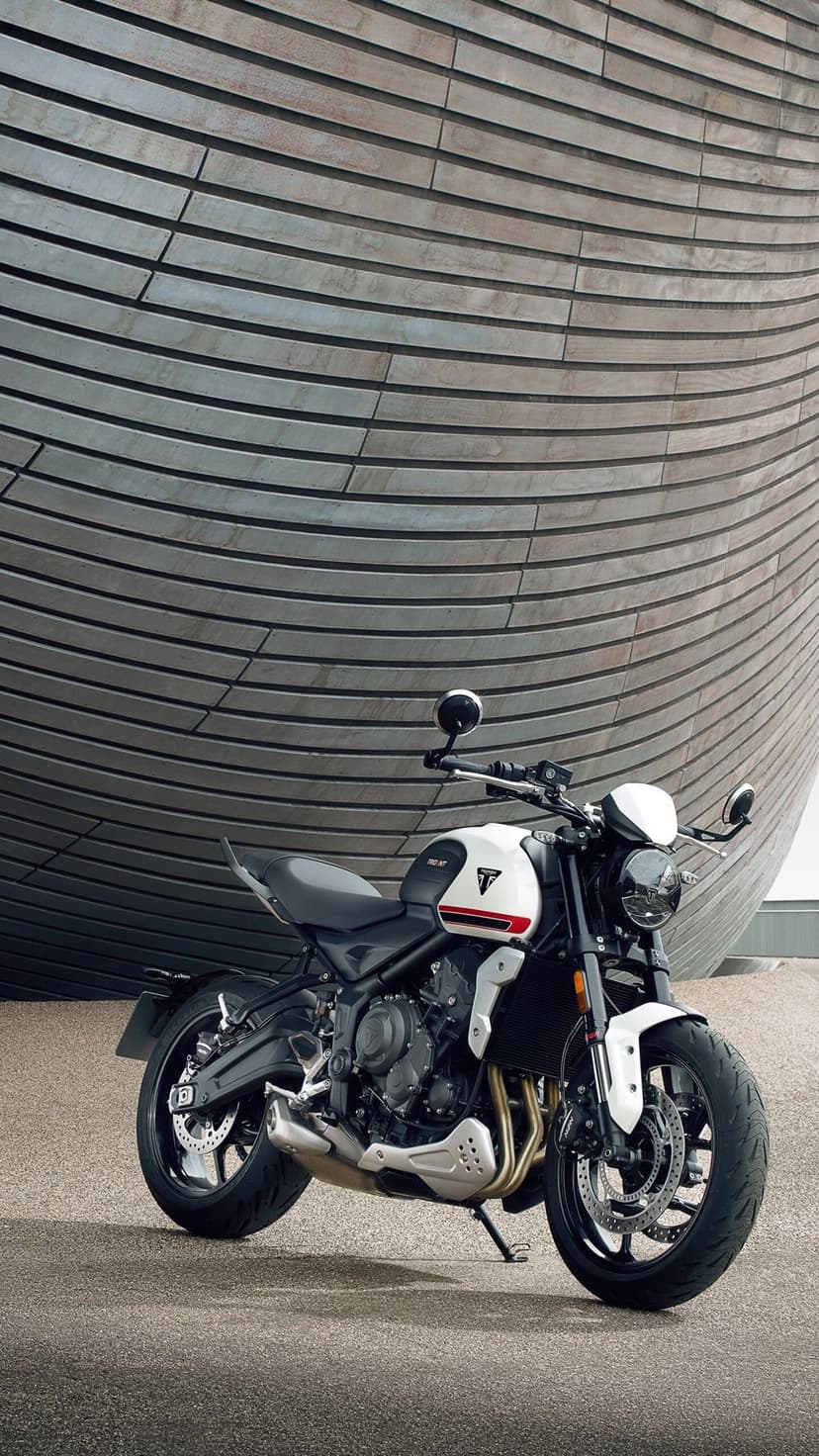 Triumph Trident 660 motorcycle parked in front of a curved metallic wall with horizontal architectural slats.