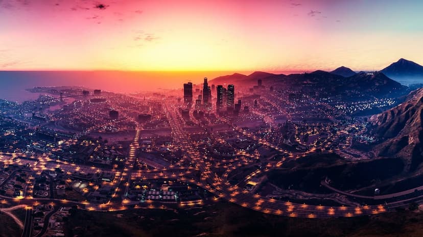 Aerial view of Los Santos at sunset with city lights glowing against a pink and orange sky with mountains.