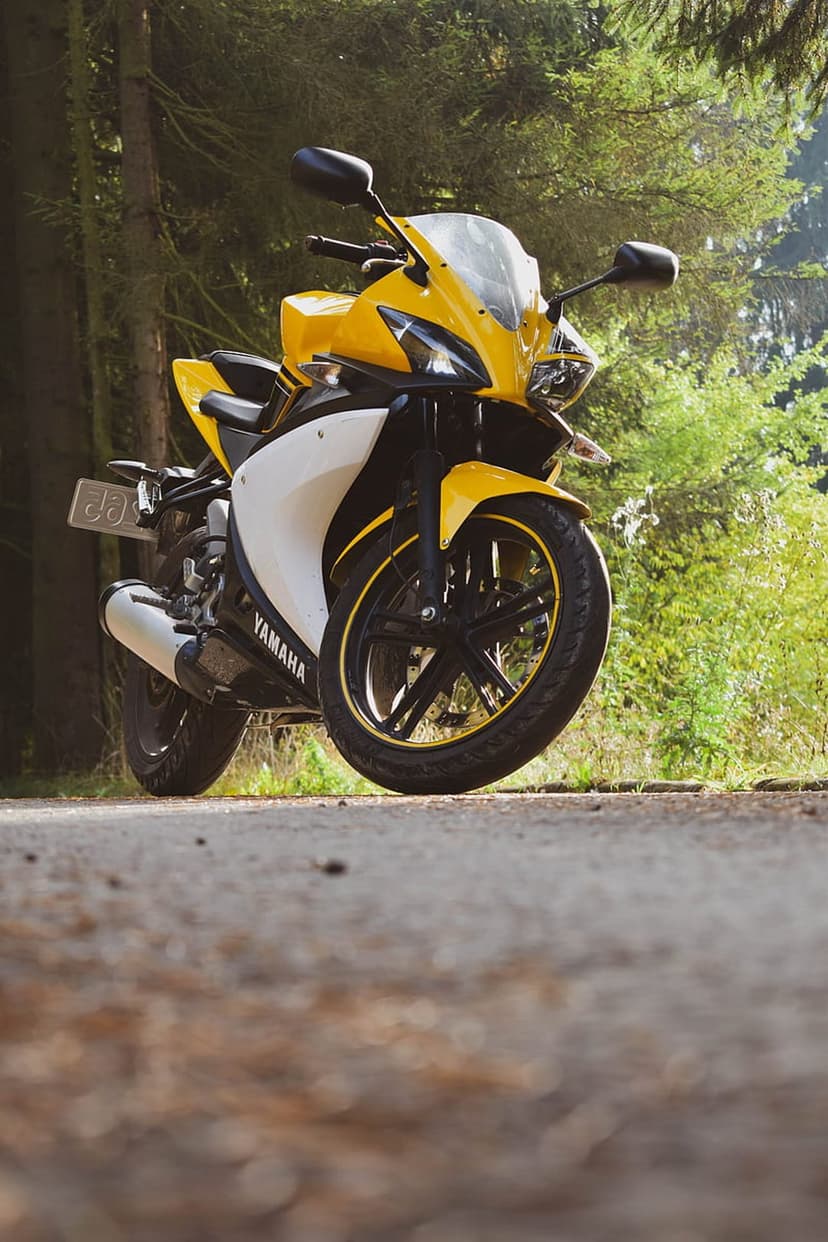 Yellow and white Yamaha motorcycle parked on an asphalt forest road with dappled sunlight hitting its fairings.