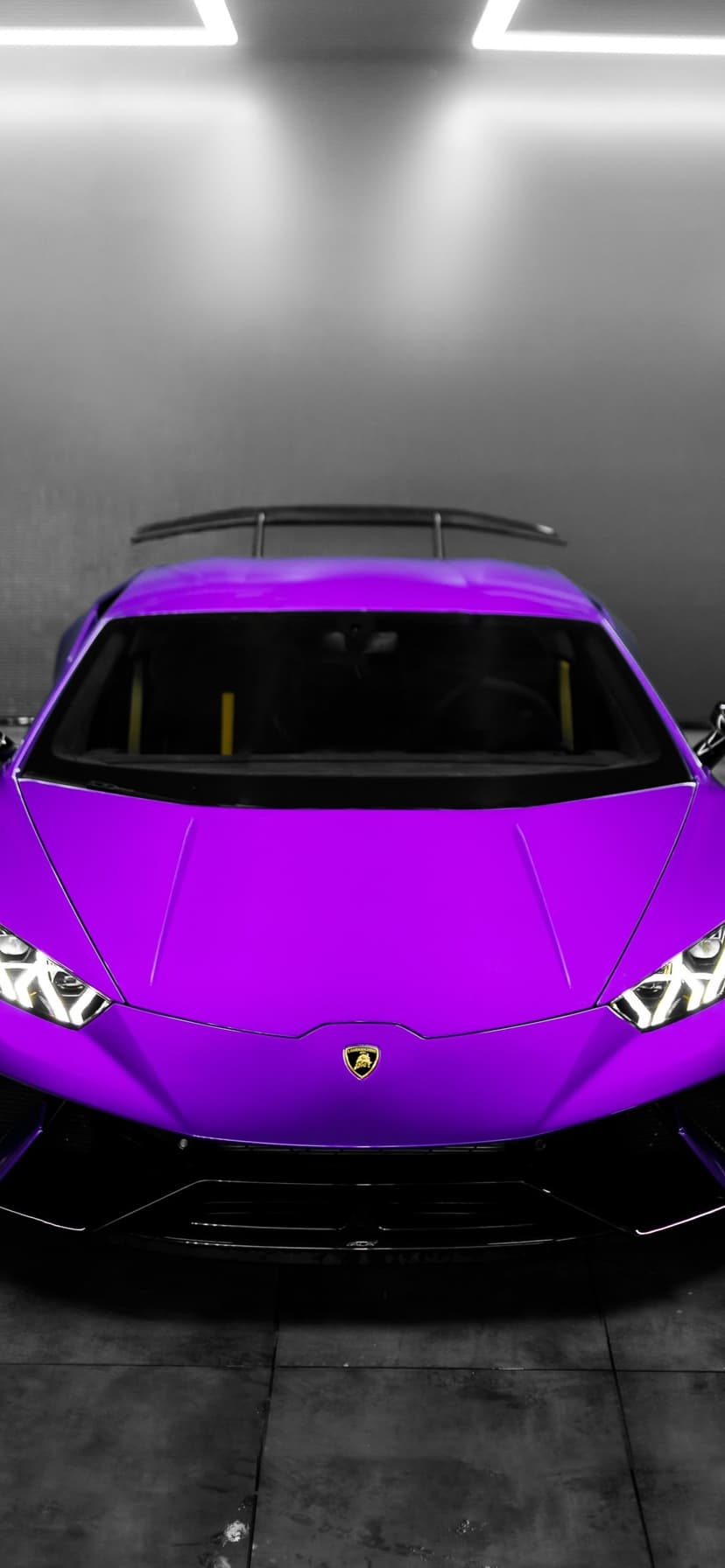 Purple Lamborghini Huracan hypercar parked in a concrete garage with sharp headlights and a rear wing spoiler.