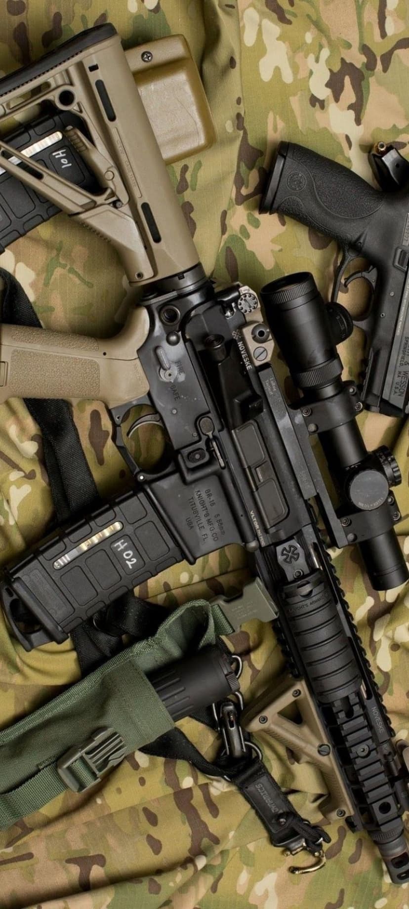 AR-15 rifle with tan stock and a black pistol resting on a green and brown camouflage patterned fabric background.