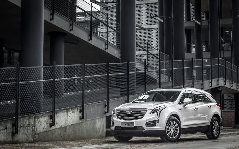 White Cadillac XT5 SUV parked in front of a modern concrete building with large black pillars and fences.