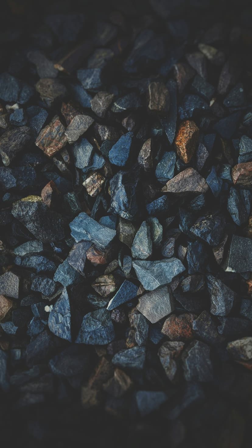 Crushed angular stones in navy blue and rusty brown hues feature sharp edges and dramatic overhead shadows.