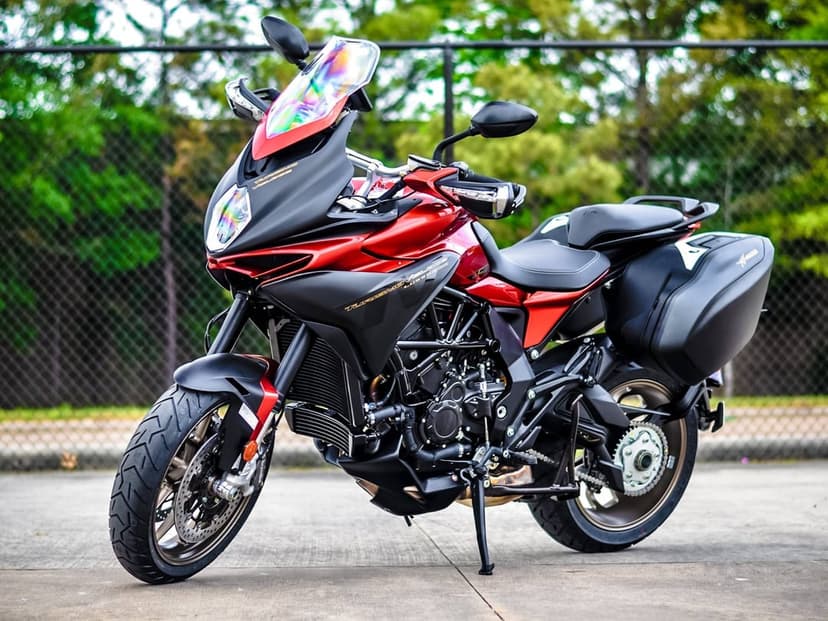 Red and black touring motorcycle with an iridescent windscreen parked on concrete against a green background.