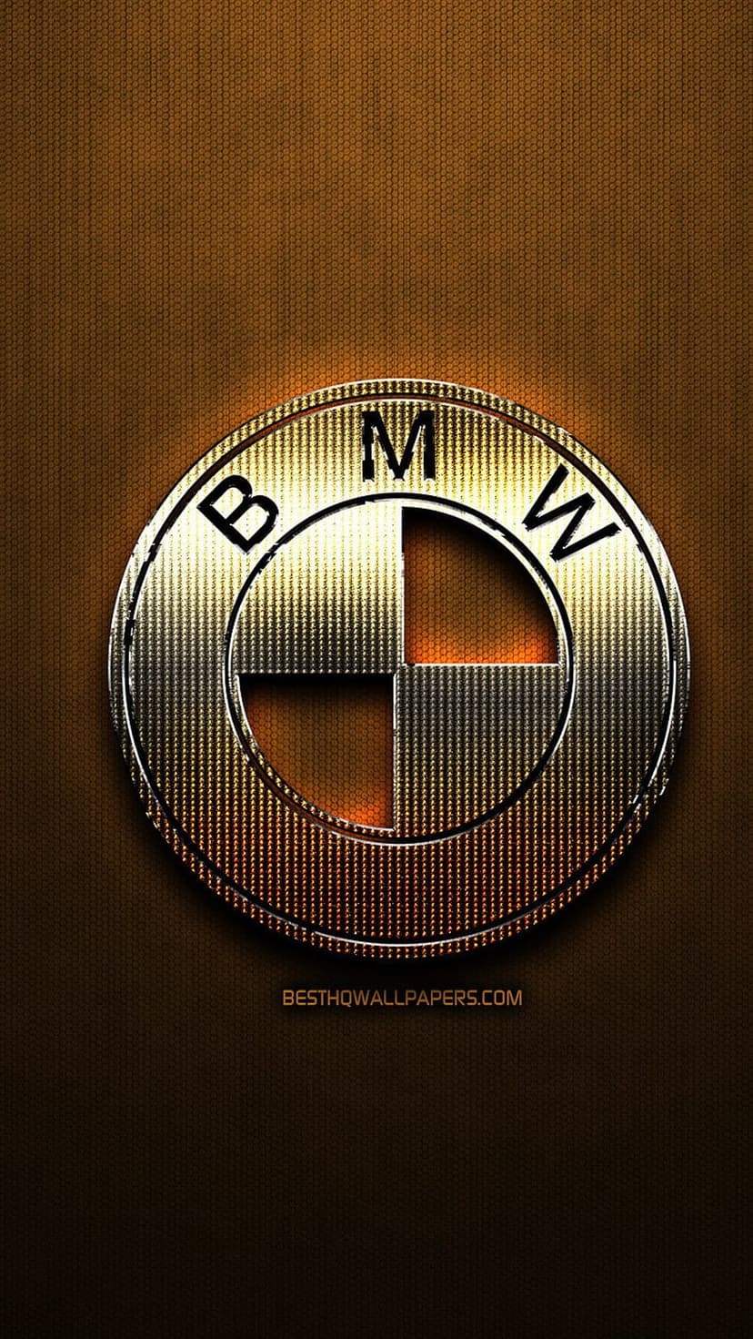 BMW logo with chrome lettering sits on a grainy brown surface, illuminated by a soft circular light effect.