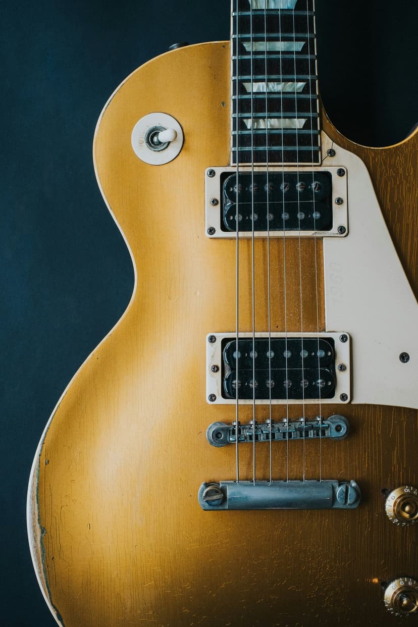 Vintage gold electric guitar with humbucker pickups and mother-of-pearl fretboard inlays on a dark backdrop.