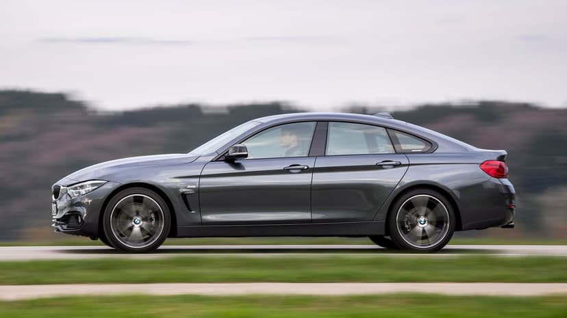 A grey BMW 4 Series Gran Coupe driving fast on a road with motion-blurred wheels and green background.