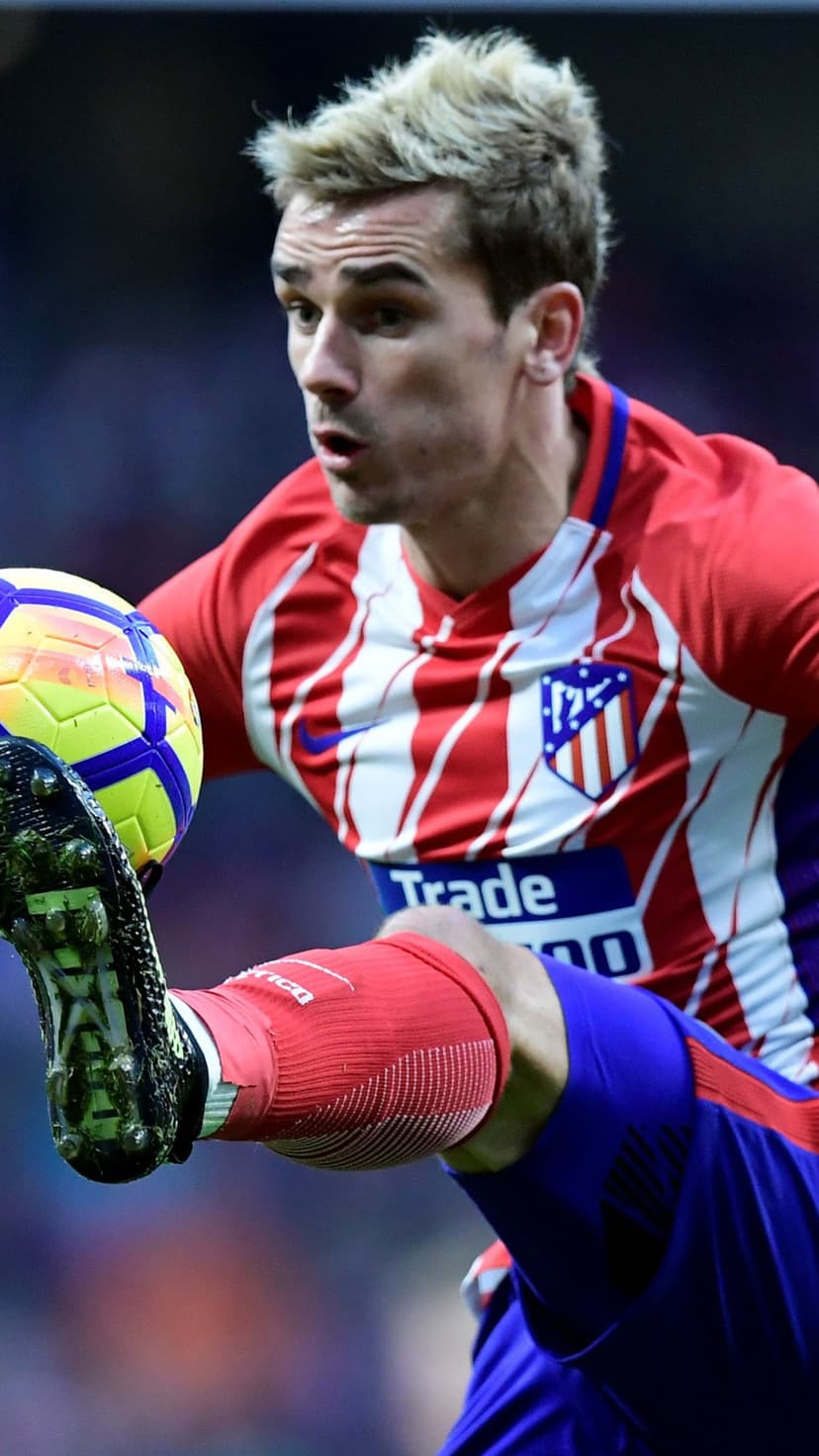 Antoine Griezmann in a red striped kit controls a football mid-air with his foot during a professional match.