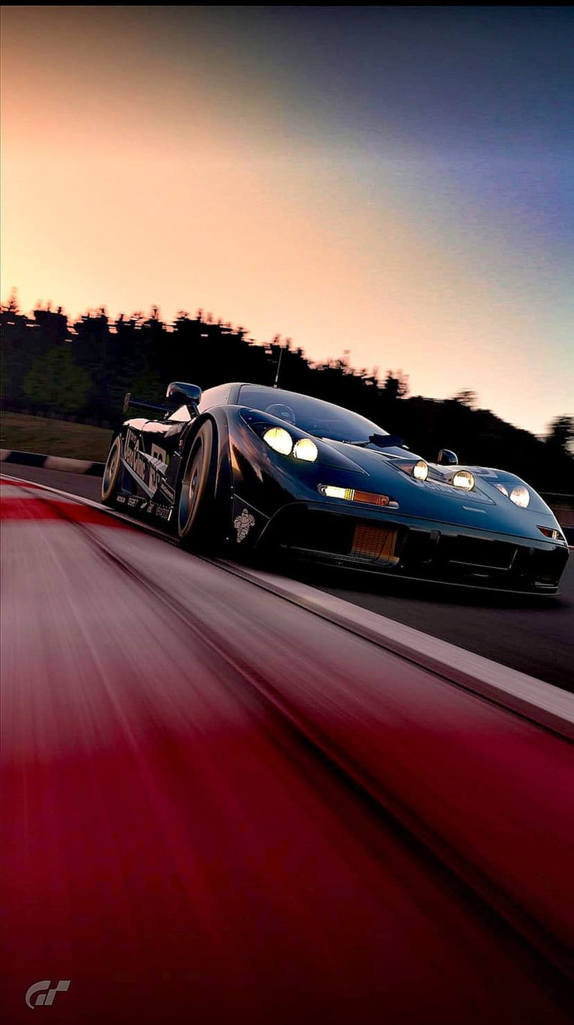 McLaren F1 GTR supercar speeds on a racetrack at sunset with glowing headlights and purple horizon clouds.