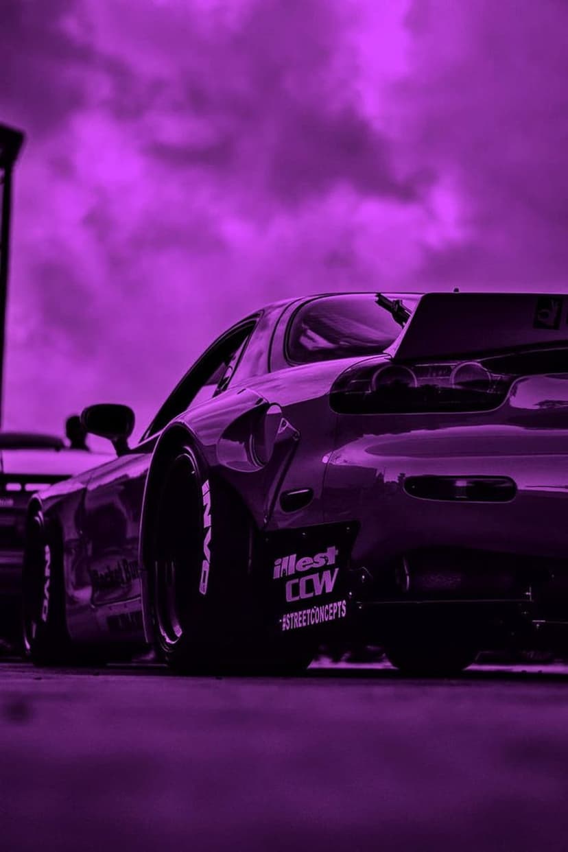 Purple Mazda RX-7 sports car with white stickers and branded tires parked under a moody violet overcast sky.