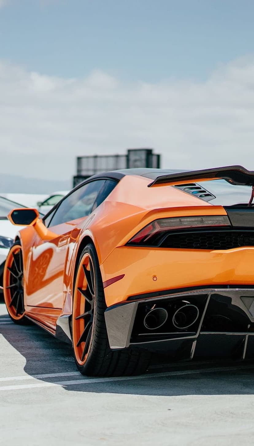 Orange Lamborghini Huracan rear view showing the spoiler, LED taillights, quad exhaust pipes, and custom wheels.