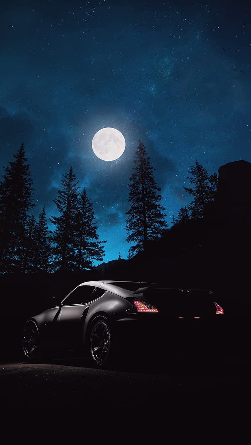 Nissan 370Z sports car parked on a dark forest road beneath a bright full moon and a glimmering starry sky.