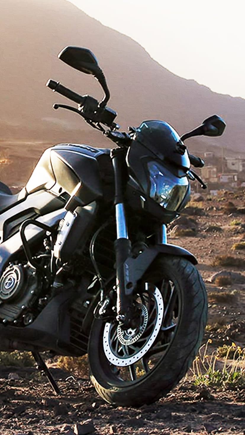 Black motorcycle with dual disc brakes parked on jagged rocks against a hazy mountain silhouette at sunset.