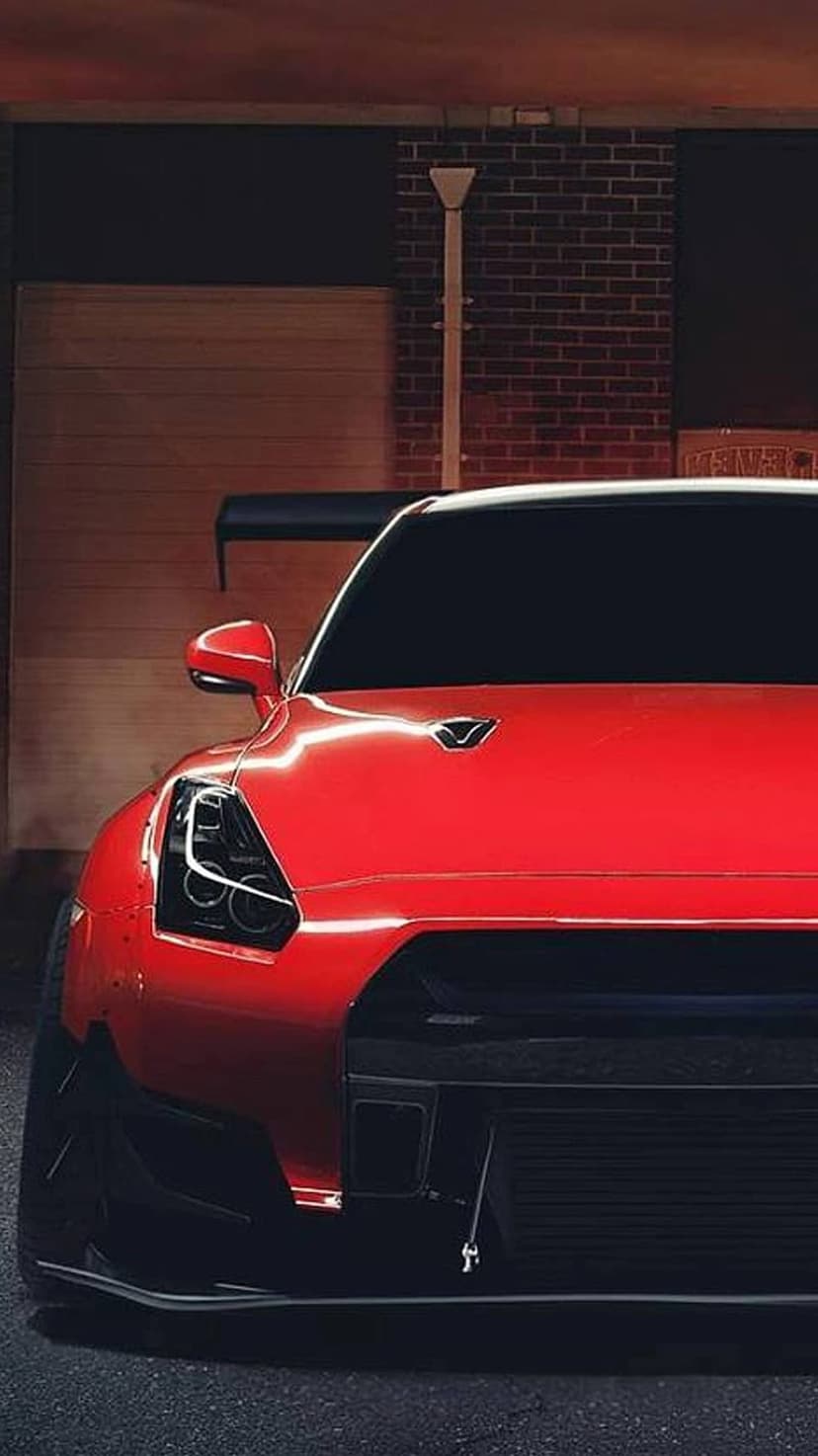 Red Nissan GT-R sports car with black spoilers and grille parked against a textured brick wall in low-angle view.