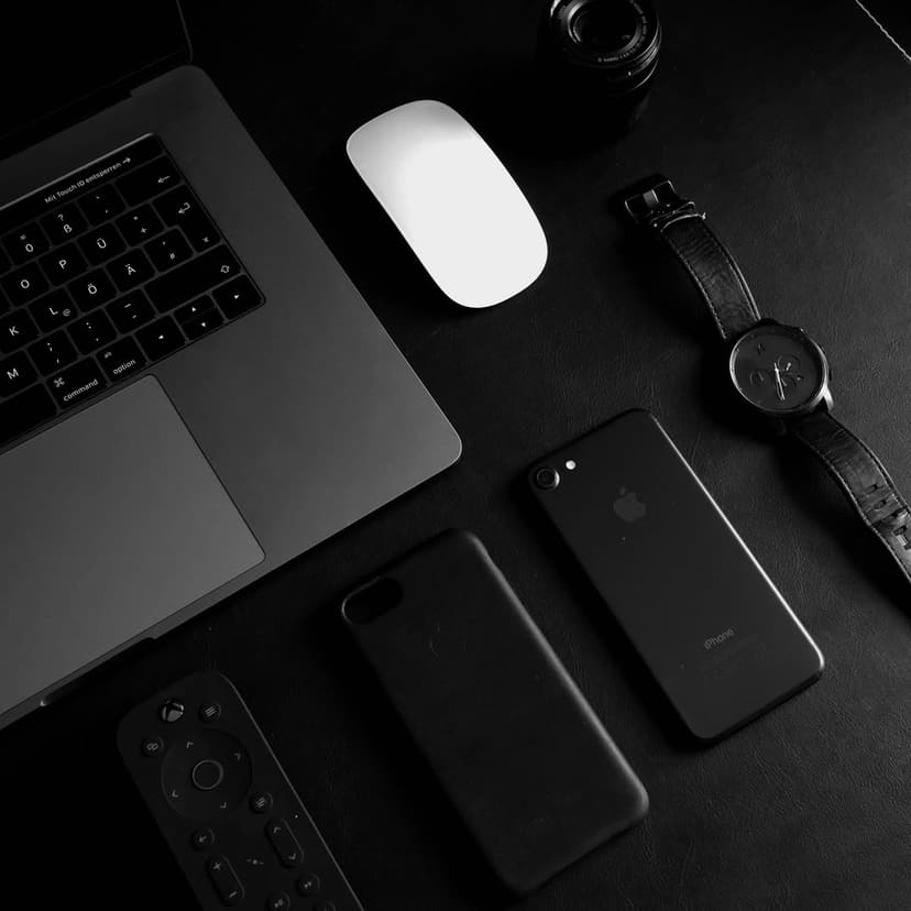 Laptop, smartphone, and smartwatch neatly aligned on a dark textured surface in a monochrome flat lay composition.