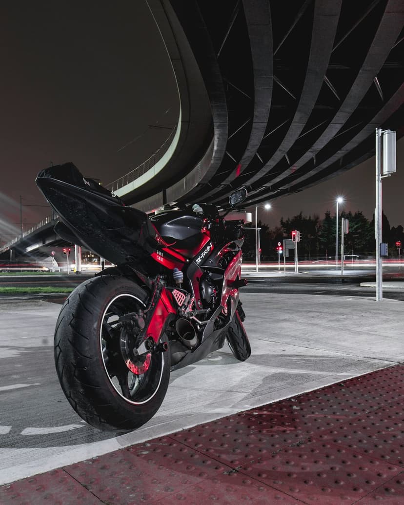 Red sport motorcycle parked under a curved concrete overpass with glowing city streetlights in the background.