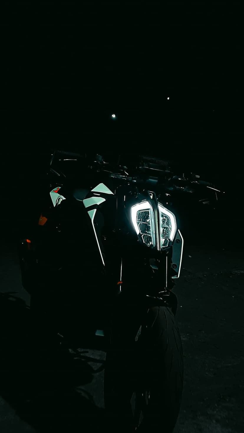 Modern motorcycle with glowing LED headlights and sharp fairings parked under two moons in a dark night setting.