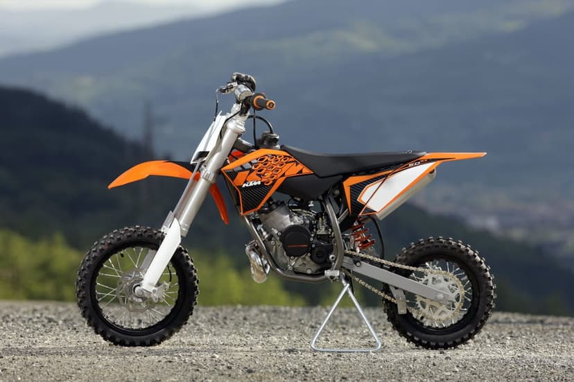 Orange and black KTM dirt bike on a gravel path with a blurred mountain range under a clear sky.