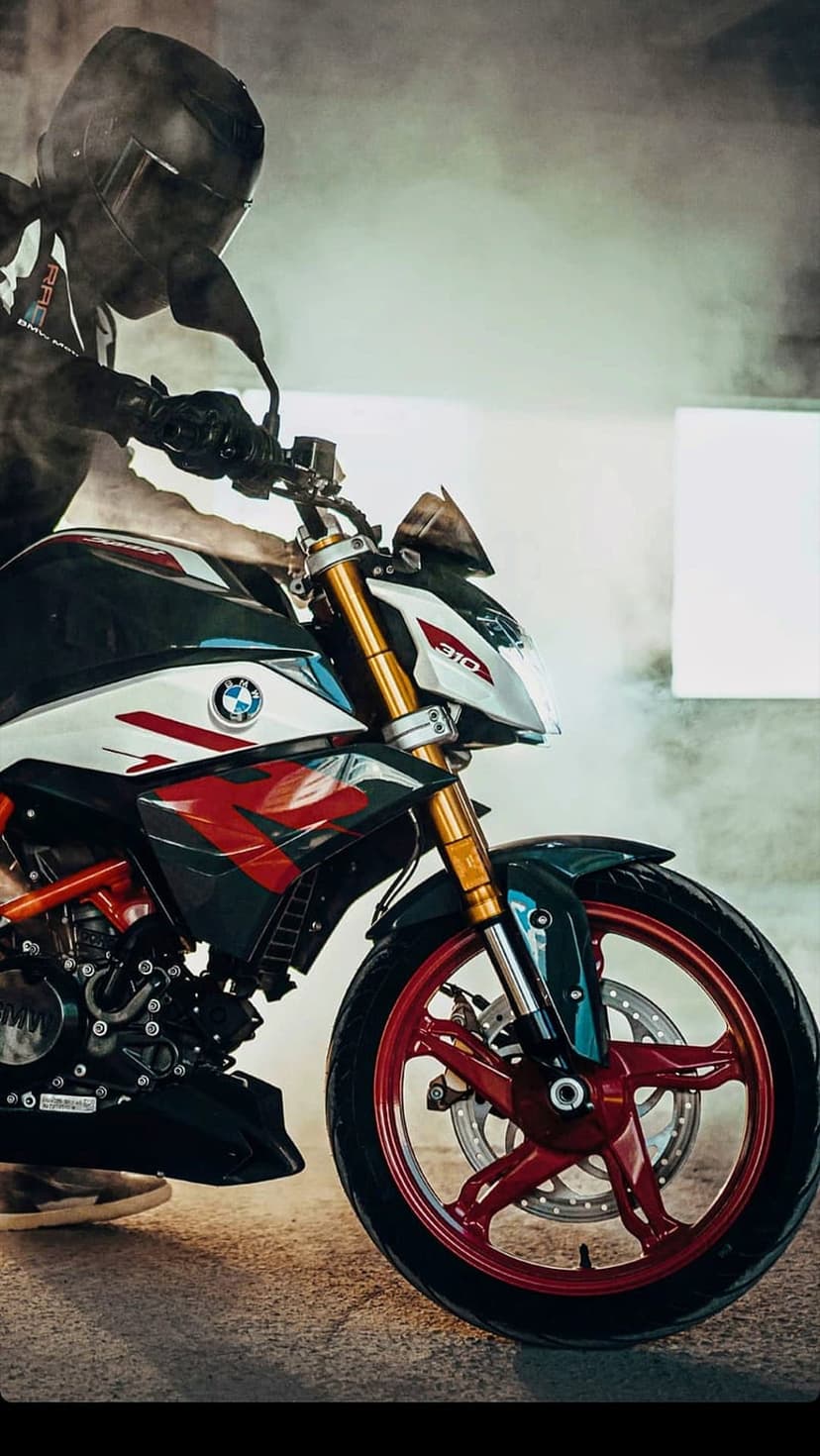 BMW motorcycle rider wearing a black helmet and gear sits on a bike with red wheels amidst thick white smoke.