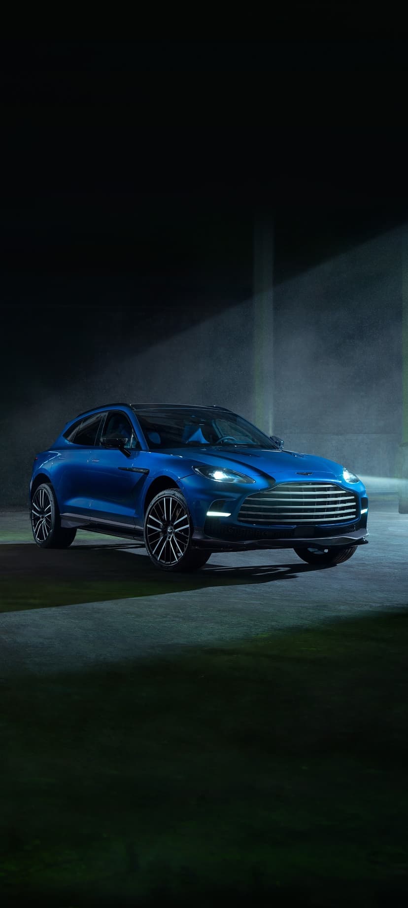 Vibrant blue luxury SUV captured in a dark, moody setting with a cinematic spotlight beam through mist.