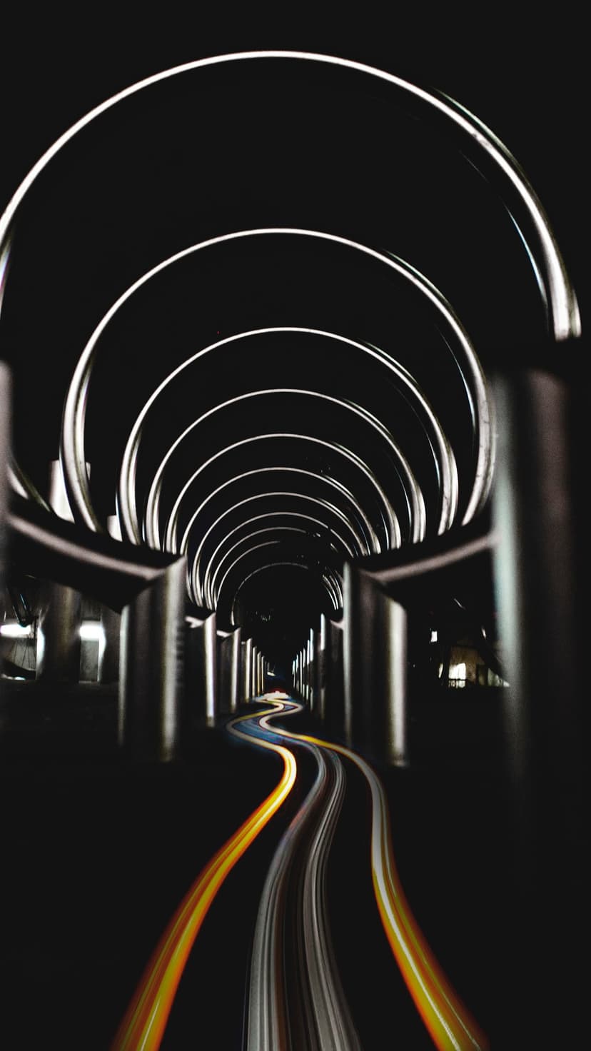 Illuminated arches form a symmetrical tunnel with blue and red light trails stretching across the dark floor.