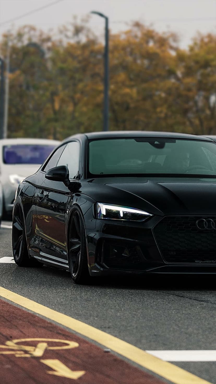 Black Audi RS5 Coupe featuring a honeycomb grille and LED headlights on a road with yellow markings.