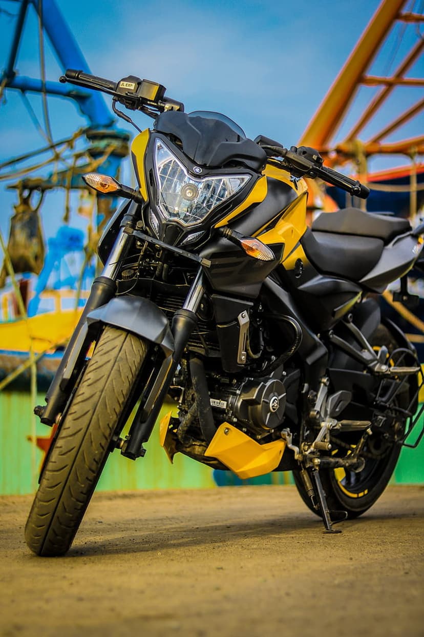 Yellow and black sport motorcycle with a prominent headlamp parked on dusty ground in an industrial harbor setting.