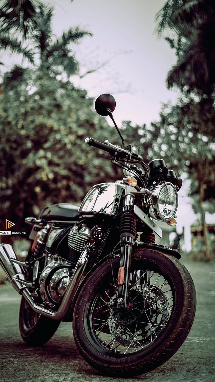 Chrome vintage motorcycle with a round headlight parked on pavement against a blurred green forest background.