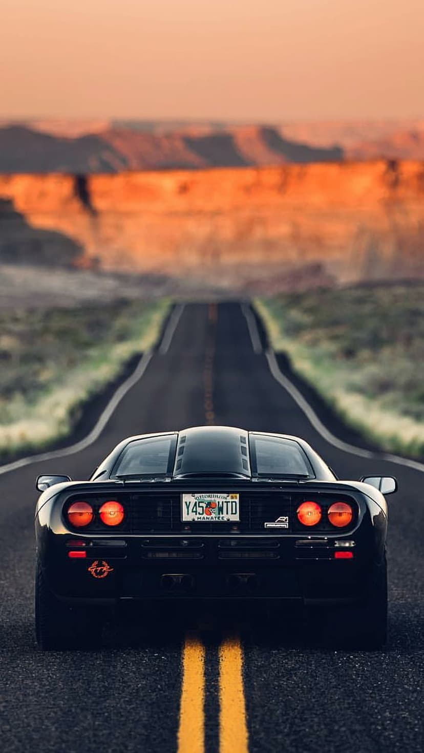 Black McLaren F1 rear view driving on a desert road during a golden sunset with glowing orange taillights.