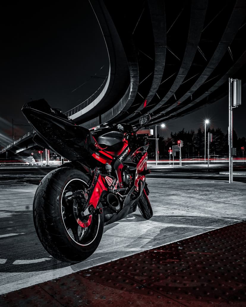 Red sportbike parked on asphalt under a concrete bridge at night with dramatic urban street lighting.