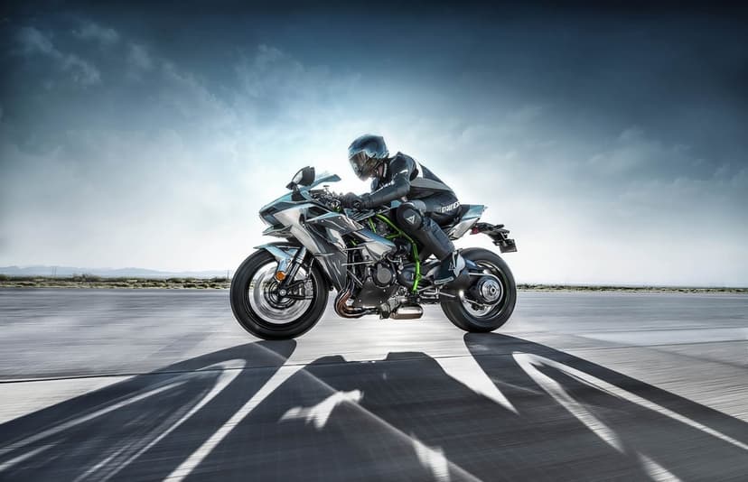 Motorcyclist in black leathers riding a silver superbike on a wide runway with long shadows and blue sky.