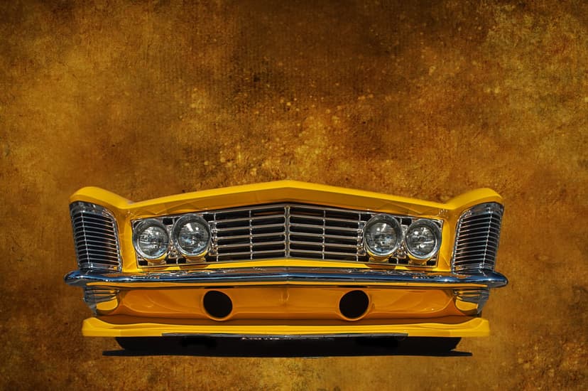 Vintage yellow car front features dual circular headlights and a polished chrome grille against a golden backdrop.