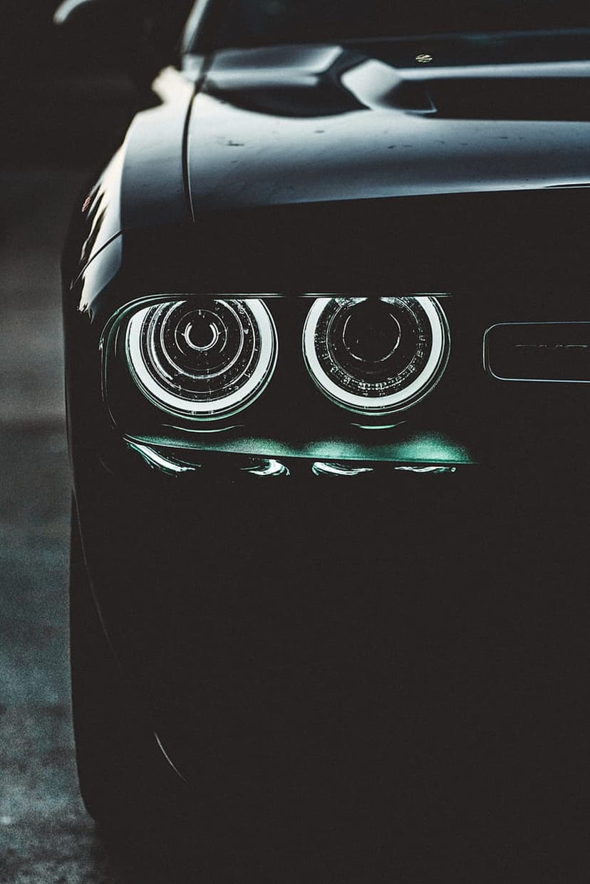 Dodge Challenger front grille and circular LED headlights glowing with teal light against a dark car body.