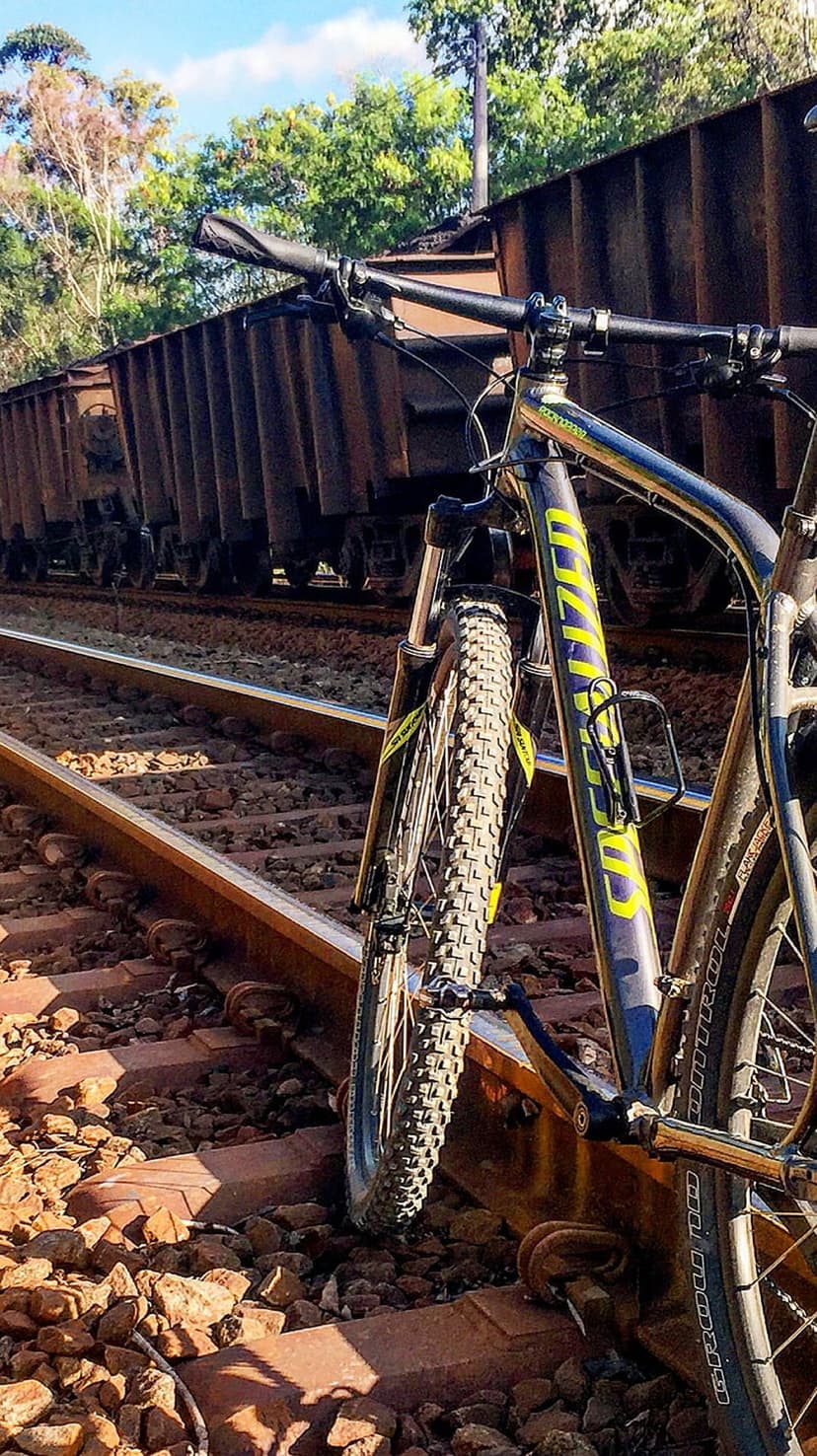 Mountain bike with yellow accents parked on steel railway tracks beside rustic brown metal freight train cars.