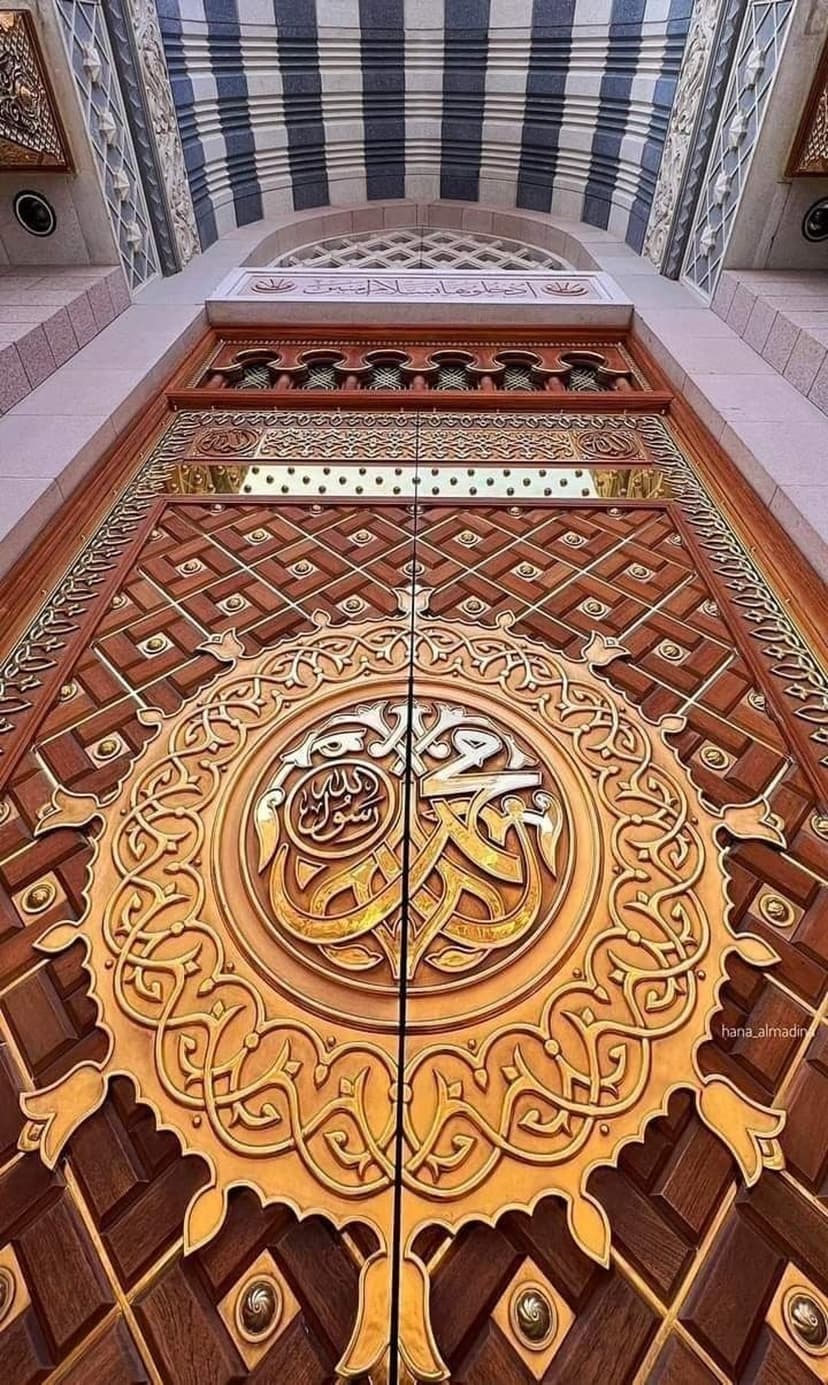 Golden Islamic calligraphy and geometric carvings on dark wooden mosque doors under soft interior lighting.