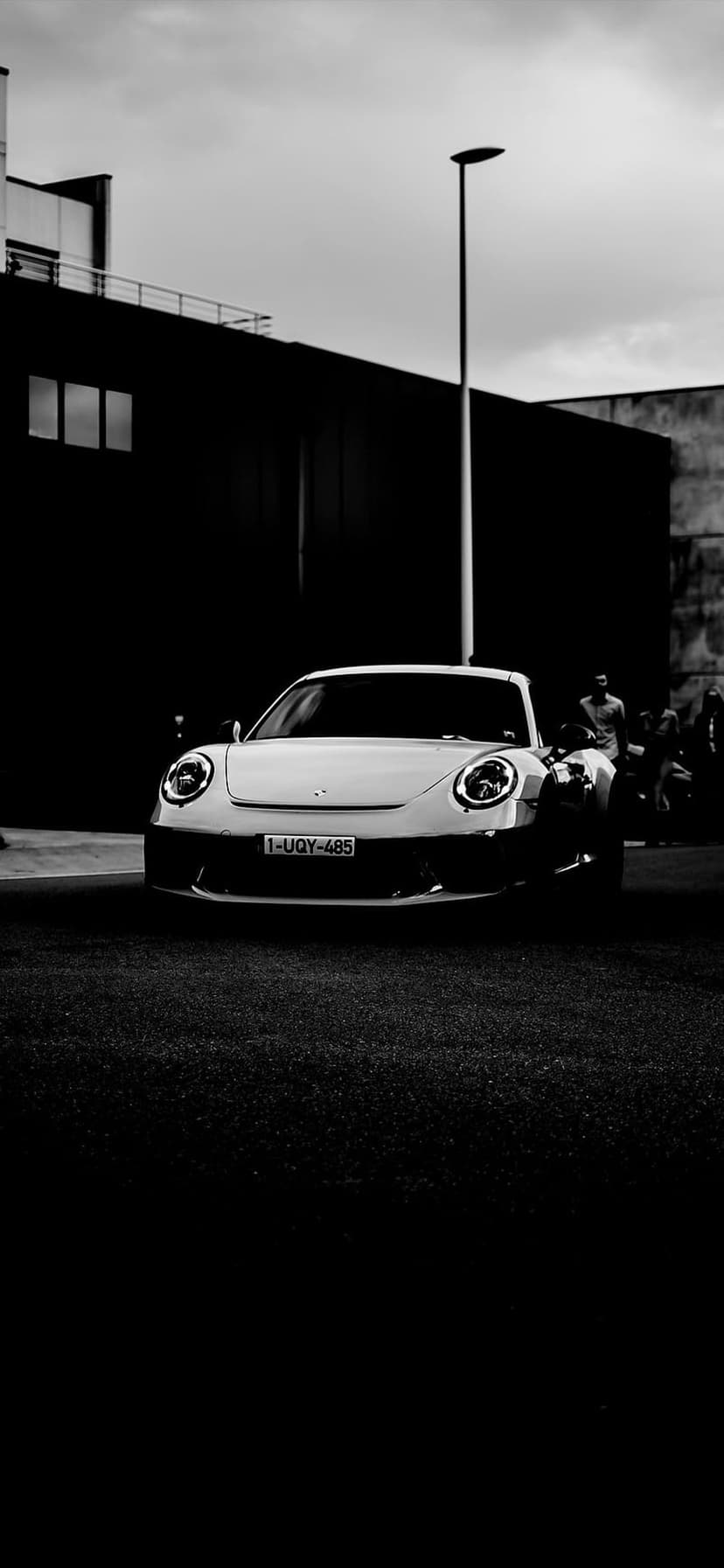 Porsche 911 parked on grass against a modern building in a high-contrast black and white photography style.