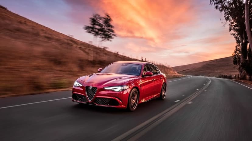 Red Alfa Romeo Giulia driving on a winding road under a vibrant orange and pink sunset sky with motion blur.